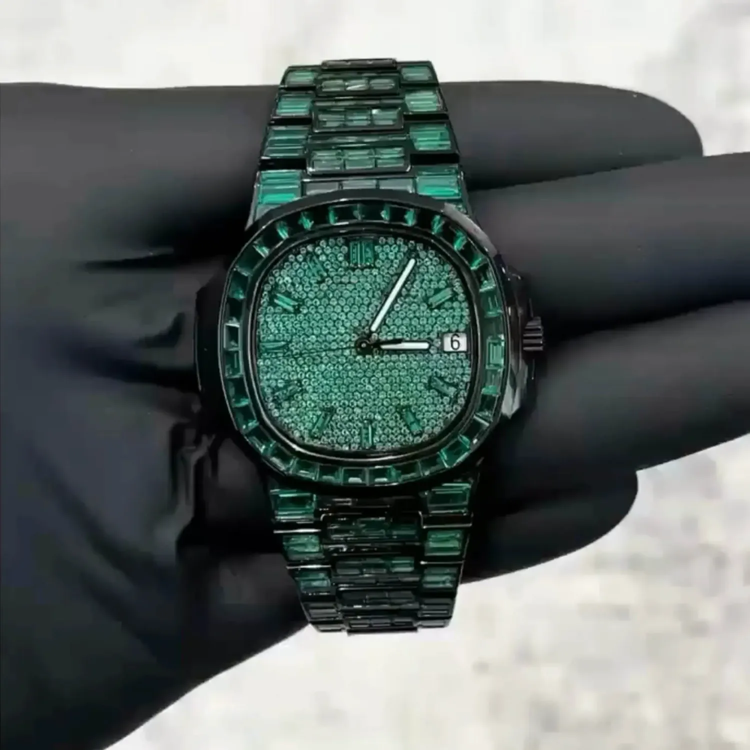 VVS1 Moissanite "Emerald" Flood: Fully handset with D-Color VVS1 Moissanite stones in a rare emerald green shade that passes thermal diamond testers. Baguette-Cut Bezel & Band: Features high-grade baguette-cut stones on the bezel and every link of the band for a clean, architectural shine. Stealth Black PVD Finish: Crafted from 316L stainless steel with a premium black PVD coating for a scratch-resistant, high-end matte-to-gloss look. Micro-Pave Dial: The watch face is fully flooded with round-cut green moissanite stones, offering 360-degree light refraction. Precision Date Function: Includes a functional date window at 3 o'clock, blending tactical utility with high-jewelry aesthetics.
