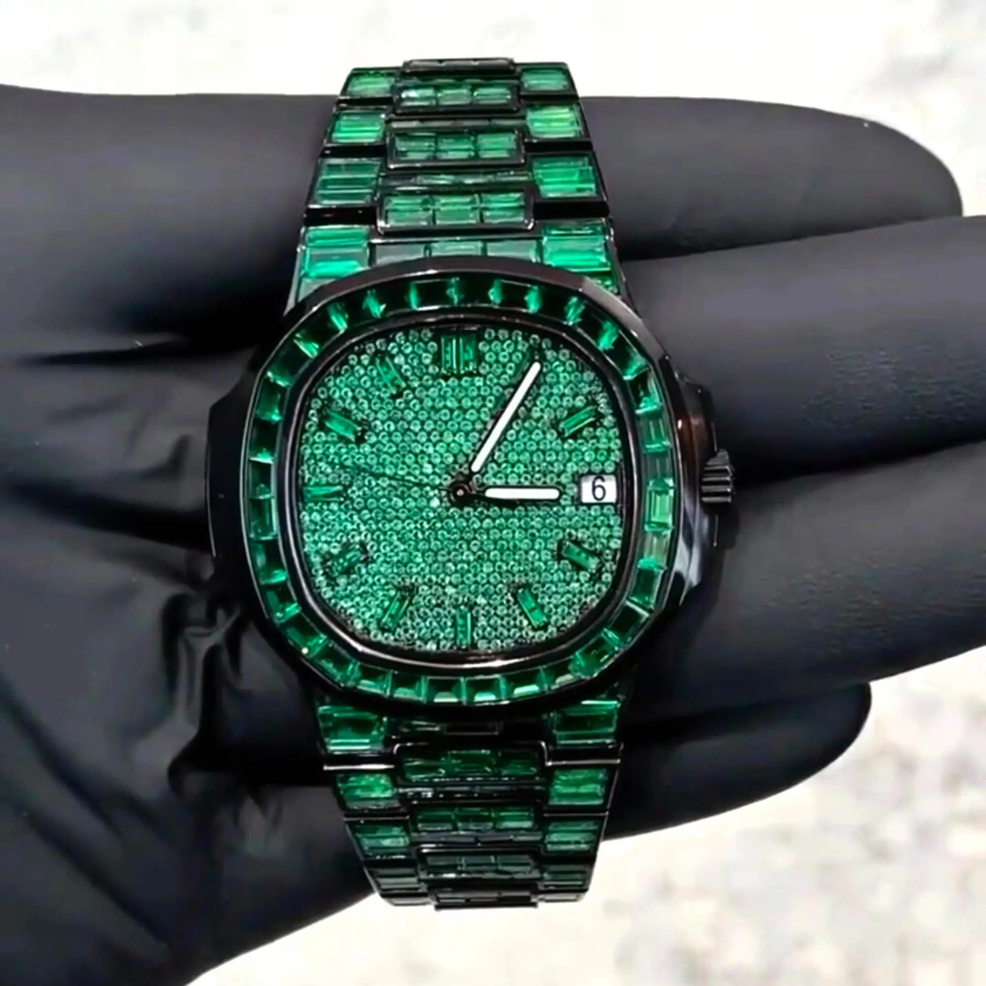 VVS1 Moissanite "Emerald" Flood: Fully handset with D-Color VVS1 Moissanite stones in a rare emerald green shade that passes thermal diamond testers. Baguette-Cut Bezel & Band: Features high-grade baguette-cut stones on the bezel and every link of the band for a clean, architectural shine. Stealth Black PVD Finish: Crafted from 316L stainless steel with a premium black PVD coating for a scratch-resistant, high-end matte-to-gloss look. Micro-Pave Dial: The watch face is fully flooded with round-cut green moissanite stones, offering 360-degree light refraction. Precision Date Function: Includes a functional date window at 3 o'clock, blending tactical utility with high-jewelry aesthetics.