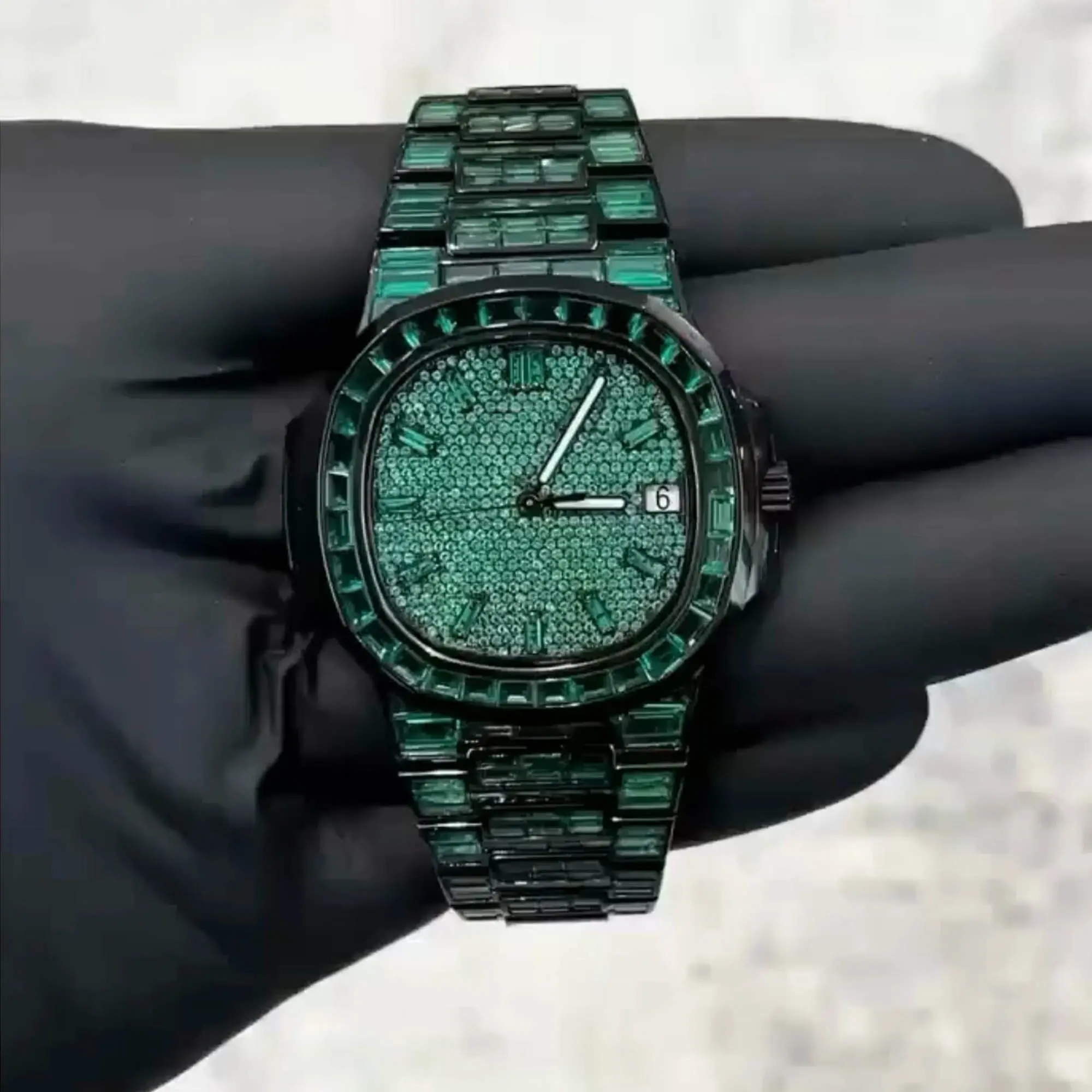 VVS1 Moissanite "Emerald" Flood: Fully handset with D-Color VVS1 Moissanite stones in a rare emerald green shade that passes thermal diamond testers. Baguette-Cut Bezel & Band: Features high-grade baguette-cut stones on the bezel and every link of the band for a clean, architectural shine. Stealth Black PVD Finish: Crafted from 316L stainless steel with a premium black PVD coating for a scratch-resistant, high-end matte-to-gloss look. Micro-Pave Dial: The watch face is fully flooded with round-cut green moissanite stones, offering 360-degree light refraction. Precision Date Function: Includes a functional date window at 3 o'clock, blending tactical utility with high-jewelry aesthetics.